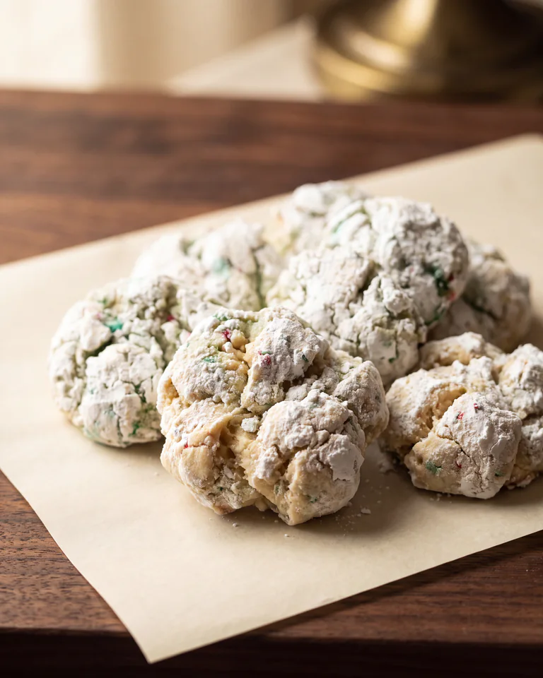 Irregular craggy Cookie Cartel knot cookies with powdered sugar and tiny colorful flecks on parchment.